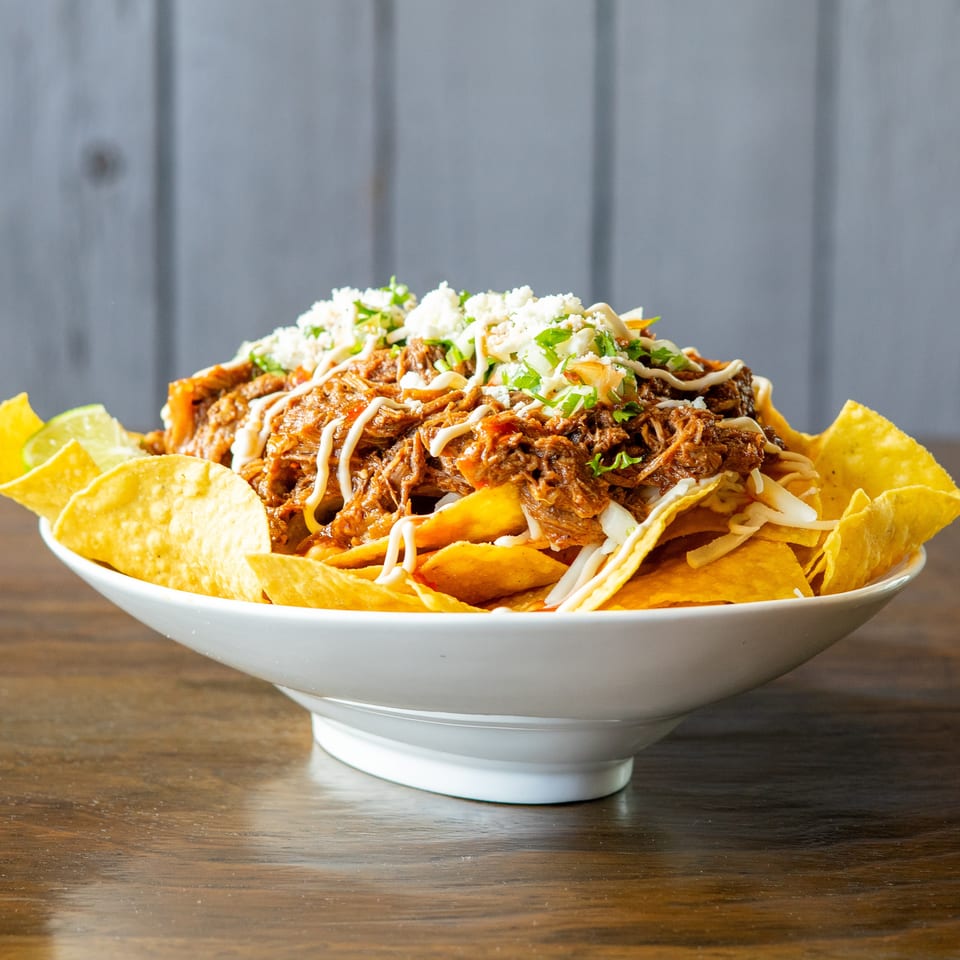 A large bowl of loaded nachos with shredded meat, cheese, and a creamy sauce.