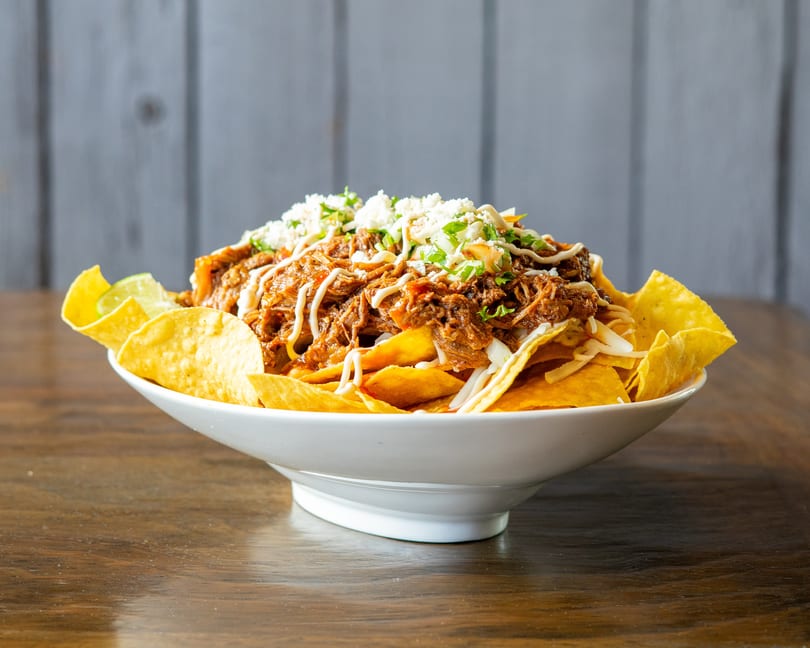 A large bowl of loaded nachos with shredded meat, cheese, and a creamy sauce.