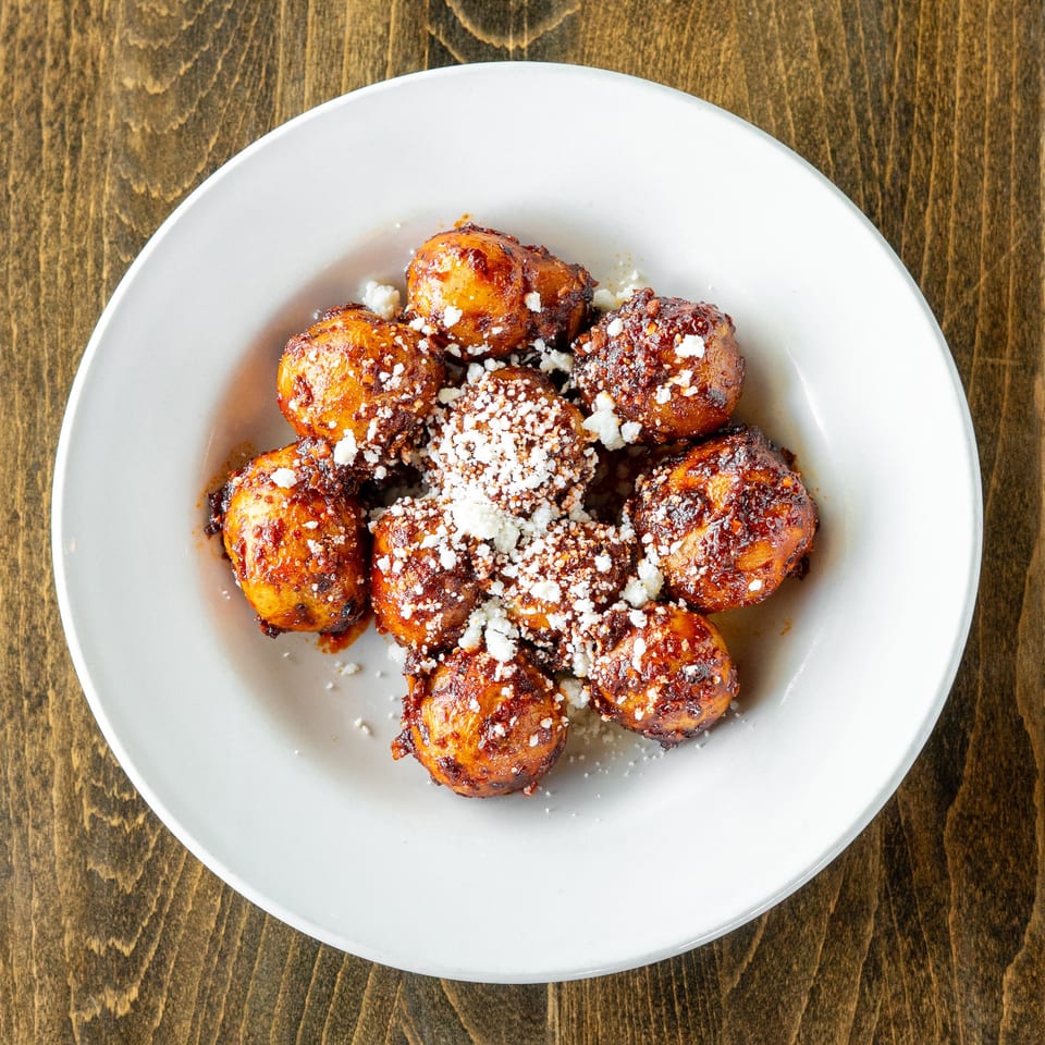 A white plate of golden-brown fried plantains, drizzled with sauce and sprinkled with white cheese.