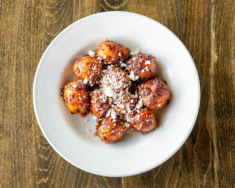 A white plate of golden-brown fried plantains, drizzled with sauce and sprinkled with white cheese.