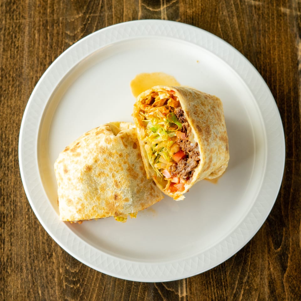 A large burrito, cut in half, revealing beef, lettuce, and tomatoes on a white plate.