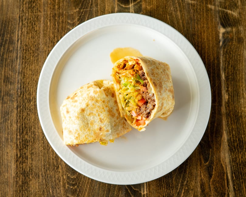 A large burrito, cut in half, revealing beef, lettuce, and tomatoes on a white plate.