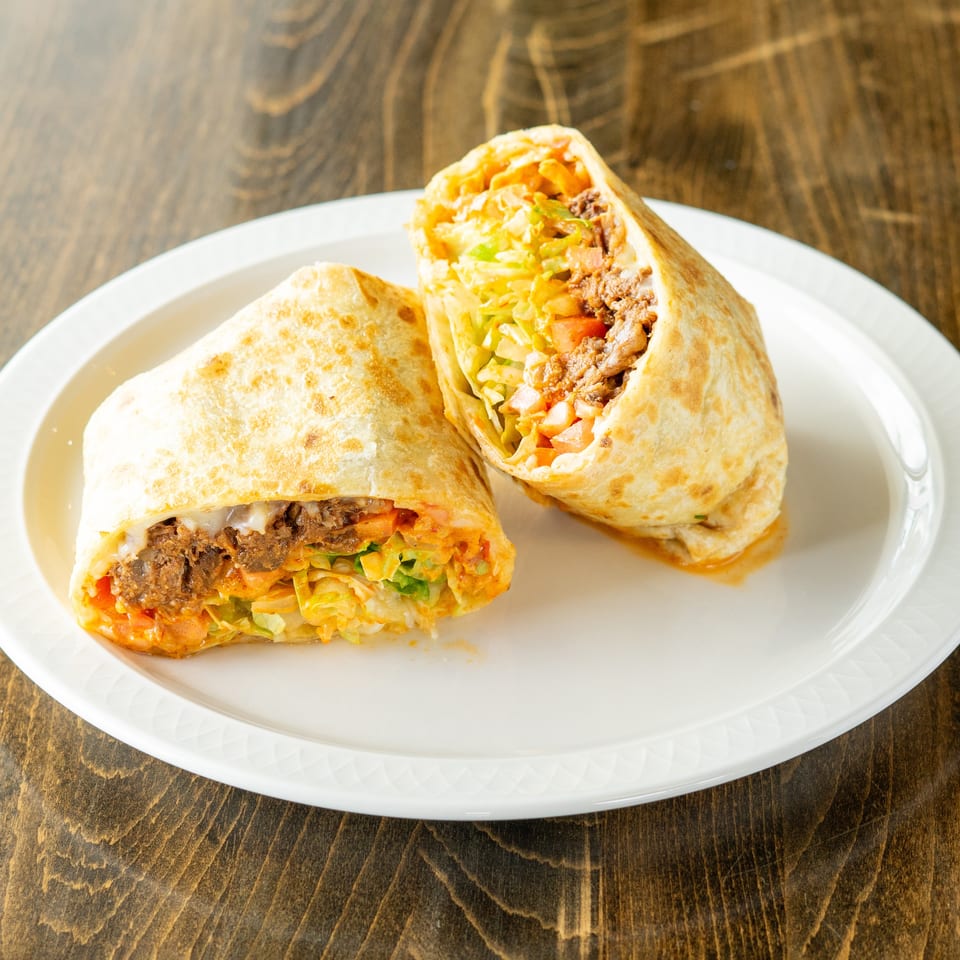 Two halves of a large burrito filled with meat, lettuce, and tomatoes on a white plate.