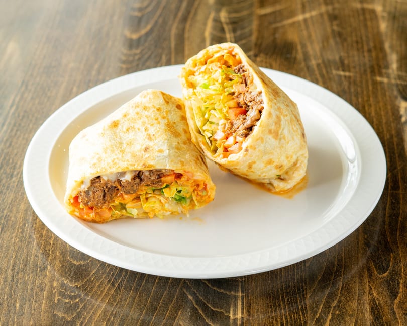 Two halves of a large burrito filled with meat, lettuce, and tomatoes on a white plate.