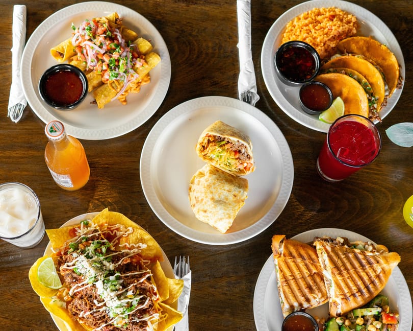 Overhead view of a wooden table laden with various Mexican dishes and drinks.
