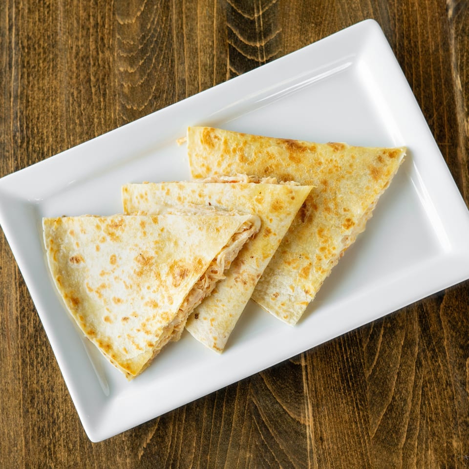 Four triangular quesadilla slices with melted cheese and chicken on a white rectangular plate.