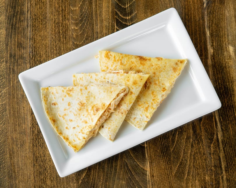 Four triangular quesadilla slices with melted cheese and chicken on a white rectangular plate.